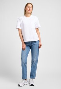 Camiseta de algodón blanca de manga corta con un bolsillo en el pecho, combinada con jeans rectos de mezclilla azul claro y zapatillas deportivas blancas.