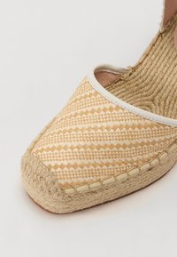 Tkané espadrilky s světle béžovým vzorem, s povrchem z provazové podrážky a bílým lemem. Texturovaný povrch s vzhledem přírodního vlákna.