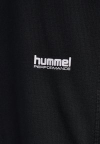 Czarna teksturowana tkanina z białym nadrukiem "hummel PERFORMANCE", prezentująca zbliżenie materiału odzieży i branding.