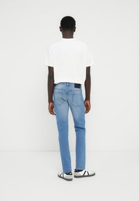 Τζιν τζιν με ελαφρύ μπλε χρώμα και ίσια γραμμή στα πόδια, διαθέτουν σκούρο λωρίδα στη μέση, συνδυασμένα με λευκό μπλουζάκι και ασπρόμαυρα αθλητικά παπούτσια.