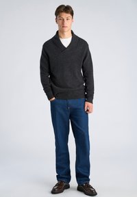 Dunkelgrauer Pullover mit Schalkragen, Strickstruktur, über einem weißen Hemd getragen. Kombiniert mit blauen Jeans und dunkelbraunen Schuhen.