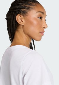 Widok z profilu osoby z warkoczami, ubrane w białą koszulę o gładkiej fakturze i okrągłym dekolcie.