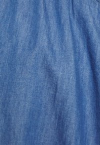 Tecido denim azul com uma textura suave, apresentando variações sutis de tonalidade e uma superfície lisa, adequado para aplicações em vestuário.