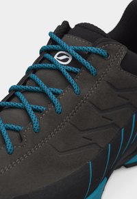 Σκούρο γκρι αθλητικό παπούτσι με υφή στην πλευρά, μπλε και μαύρα κορδόνια με σχέδιο και μαύρη σόλα με μπλε λεπτομέρειες.