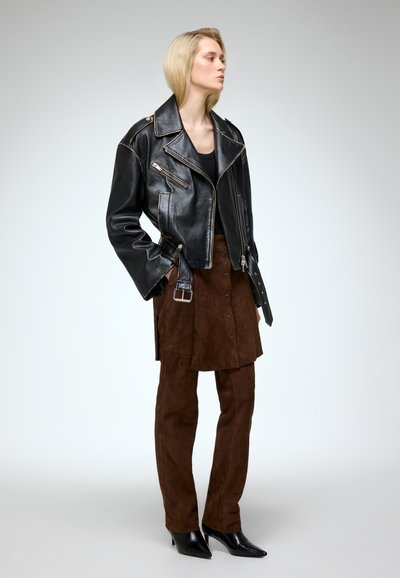 Black leather motorcycle jacket with silver hardware, paired with a brown suede skirt and matching trousers, complemented by pointed black boots.