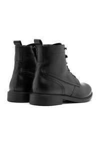 Botas de cuero negras hasta el tobillo con una textura suave, cordones en la parte delantera y cremallera lateral. Presentan un tacón bajo y sólido con diseño de punta redondeada.