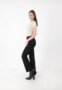 Top beige ajustado, jeans negros de tiro alto, corte estilizado, botas de tacón negro puntiagudas, tejido suave, diseño sencillo, estilo minimalista.