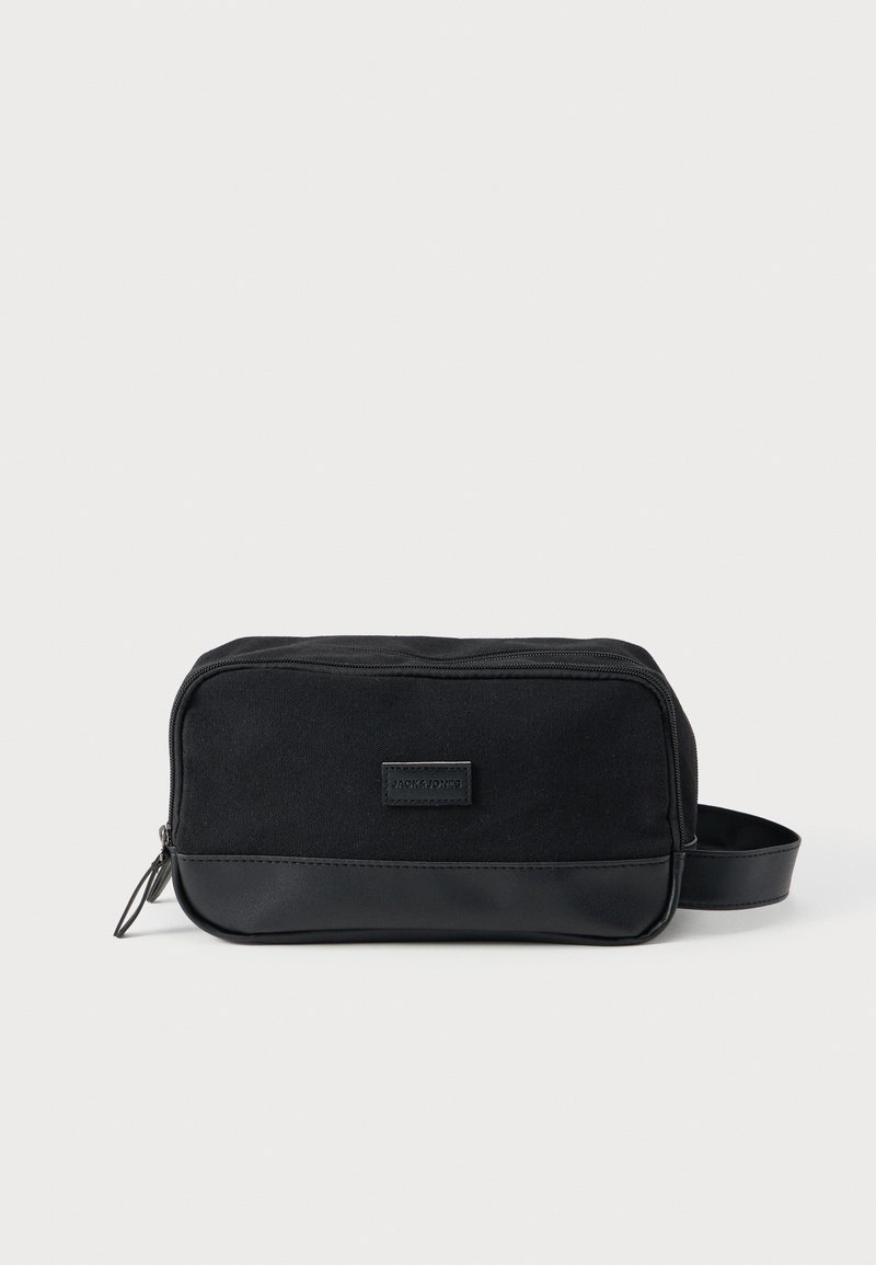 Συμπαγής μαύρη τσάντα καλλυντικών με υφασμάτινο σώμα, δερμάτινη βάση, επάνω φερμουάρ και πλαϊνή λαβή σε απλό φόντο.