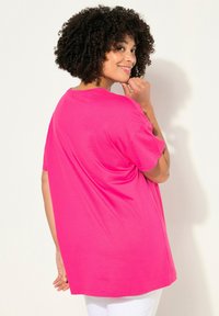 Camiseta oversized de color rosa brillante con mangas cortas y cuello redondeado, hecha de una tela suave, que presenta un corte relajado y aberturas laterales.