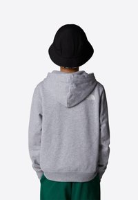 Felpa grigia con cappuccio dalla texture morbida, cappuccio regolabile e logo sulla parte superiore della schiena, abbinata a un cappello a secchiello nero.