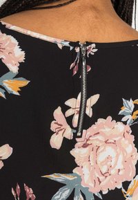 Sorte stof med pink og gule blomsterdesigns, med en metal lynlås detalje bagpå og en glat tekstur.