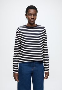 Cămașă cu dungi, cu mâneci lungi în bleumarin și alb, cu decolteu rotund și croială lejeră, asortată cu pantaloni din denim albastru.