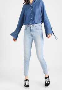 Vaaleansiniset farkut, kapeat malli, yhdistetty tumma sininen napituspaita, jossa on levenevät hihat, sekä mustat tennarit.