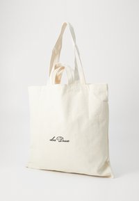 Canvas tote veske i kremfarge med to robuste håndtak og frontlogo "Les Deux" i mørk skrift. Enkel, rektangulær form med glatt tekstur.