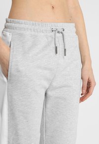 Hellgraue Baumwollmischung-Sweatpants mit elastischem Bund, Kordelzug, Seitentaschen und kontrastierenden Seitenpaneelen. Glatte Textur.