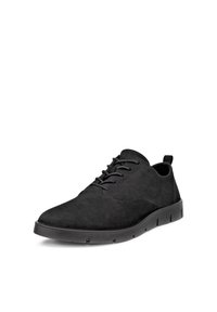 Chaussure décontractée noire en daim à lacets, bout arrondi, semelle épaisse et flexible, avec languette au talon, présentée légèrement inclinée sur fond blanc.