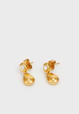 Złote kolczyki wkręty z przezroczystym akcentem w postaci rhinestone, z teardropowym zawieszeniem wiszącym poniżej kolczyka, o gładkim, błyszczącym wykończeniu.