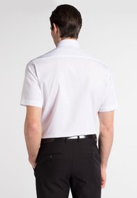 Hvid kortærmet skjorte med klassisk krave, glat stof og en lige bagside, parret med sorte dressbukser og et bælte.