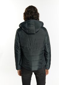 Mörkgrön isolerad jacka med huva, som har en quiltad design och mjuk textur. Bakifrån syns sömmarna och den skräddarsydda passformen.