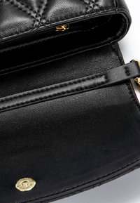 Zwarte leren handtas met een gequiltde textuur, gouden hardware en een ritscompartiment. Heeft een gladde, gedetailleerde binnenvoering.