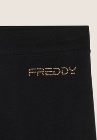 Leggings negros con una textura suave. Presentan un diseño de logo con tachuelas doradas en la cintura, destacando el nombre de la marca "FREDDY."