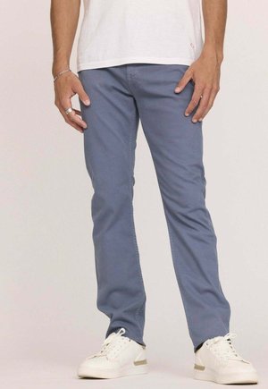 Chinos en coton bleu clair de coupe slim, avec poches arrière, portés avec des baskets blanches. Style simple et décontracté.
