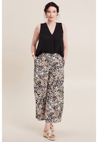 Top nero senza maniche con scollatura a V, abbinato a pantaloni a gamba larga con una stampa di foglie nera e beige. Il modello indossa sandali con zeppa dorati.