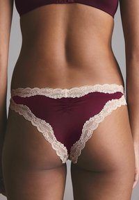 Bordeaux kanten randje string, gemaakt van zachte elastische stof, met een delicate crème kanten rand langs de taille en randen, die het ontwerp versterkt.