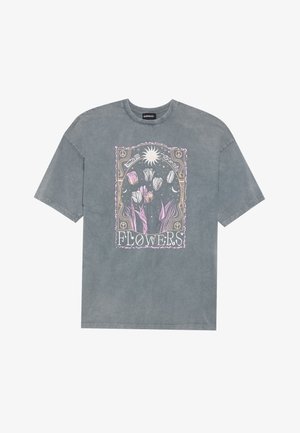 Szürke, oversized póló színes virágmintával, rajta a "FLOWERS" felirattal. A design pasztell árnyalatokat és díszítőelemeket tartalmaz.