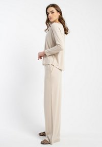 Beżowa bluzka z długim rękawem i dopasowane spodnie o szerokich nogawkach, wykonane z gładkiego, lekkiego materiału. Całość dopełniają charakterystyczne klapki w panterkę.