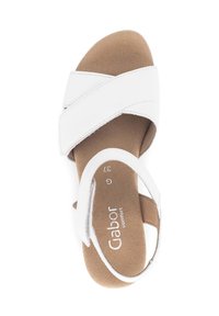Sandal in pelle bianca con cinghie incrociate, soletta imbottita, suola flat e cinturino alla caviglia regolabile con una soletta marrone texturizzata.