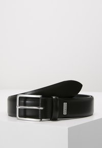 Cinturón de cuero negro con una textura suave, que presenta una hebilla de metal plateado y un acento de logo. El diseño es simple y clásico en su forma.
