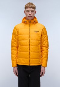 Gelbe Plüschjacke mit Kapuze, Reißverschluss und sichtbaren Nahtlinien. Markenlogo auf der Brust, Stoff mit glatter Textur.