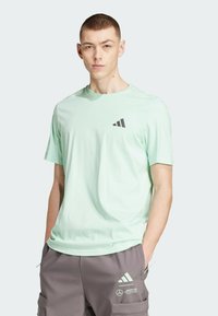 Camiseta de cuello redondo en un suave verde menta, confeccionada con tela suave, presenta un pequeño logo negro en el pecho y mangas cortas.