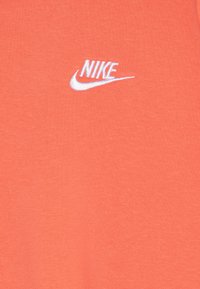T-maica v koralni barvi, izdelana iz mehkega bombažnega materiala, z belim vezenim logotipom "NIKE" na levem prsnem delu.