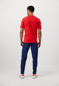 Κόκκινη κοντομάνικη μπλούζα συνδυασμένη με ναυτικές αθλητικές παντελόνες. Το σύνολο έχει στρογγυλή λαιμόκοψη και άνετη εφαρμογή. Λευκά αθλητικά παπούτσια με κόκκινες λεπτομέρειες.