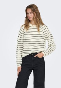 Pull couleur crème avec des rayures noires, doté d'un col rond et de manches longues, associé à un jean noir taille haute.