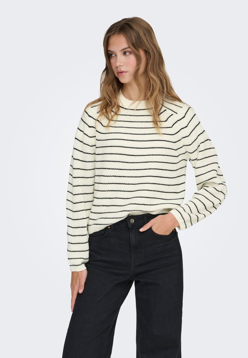 Pull couleur crème avec des rayures noires, doté d'un col rond et de manches longues, associé à un jean noir taille haute.