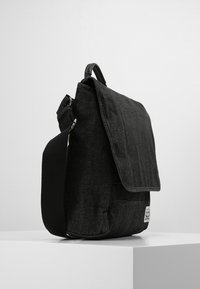 Bolso mensajero de mezclilla negra con cierre de solapa, con un acabado texturizado y un bolsillo frontal, correa ajustable y etiqueta de marca.