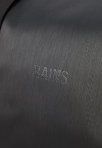 Črn vodoodporen nahrbtnik z teksturirano površino in navpičnimi črtami ter odtiskanim logotipom "RAINS". Preprost, eleganten dizajn z mat površino.