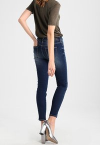 Sisir jeans ramping dalam denim biru tua, memiliki pinggang tengah, pudar halus, dan saku belakang. Dipadukan dengan sepatu hak tinggi perak.