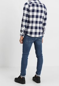 Granatowa i biała w kratkę flanelowa koszula z długim rękawem, w zestawieniu z wąskimi niebieskimi dżinsami i czarnymi sneakersami. Widoczne detale mankietu.