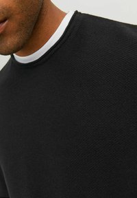 Maglione nero a trama con collo a girocollo, caratterizzato da un colletto interno bianco a contrasto. Primo piano che mostra i dettagli del materiale e le caratteristiche del design.