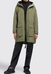 Olivgrön parkajacka med huva, framdragkedja, två stora framfickor och justerbar midja. Gjord av glatta, lätta material.