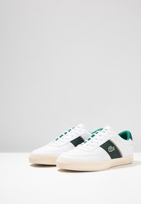 Bílé tenisky s akcenty v zelené a tmavě zelené barvě. Vyrobené z syntetického materiálu, s texturovaným povrchem a šněrovacím designem.