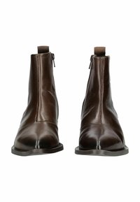 Stivali ankle in pelle marrone con una texture liscia, punta affusolata e cerniere laterali. Design minimalista con tacco basso e profilo elegante.
