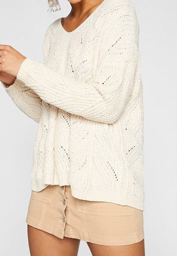 Un pull en laine de couleur crème à coupe ample, avec des motifs ajourés et des poignets côtelés, associé à une jupe beige à boutons sur le devant.