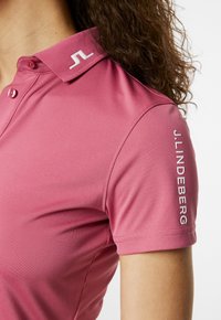 Roze polo met kraag, met een wit logo op de kraag en de mouw. Glad, atletisch materiaal, korte mouwen, slim fit ontwerp.