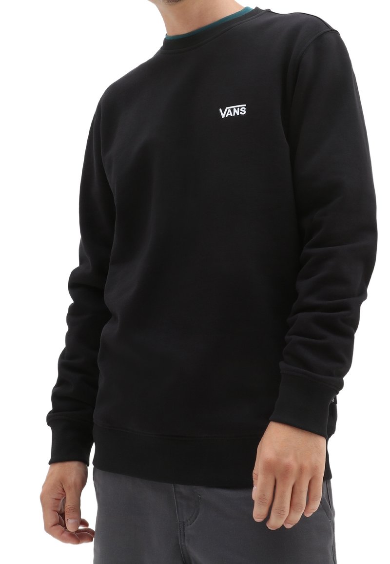 Felpa nera a girocollo in misto cotone, con logo Vans bianco sul petto, polsini a costine e un design scuro uniforme.