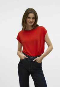 Haut rouge à manches courtes avec une coupe décontractée, associé à un jean en denim bleu foncé avec une taille et des poches. Texture lisse, look décontracté.